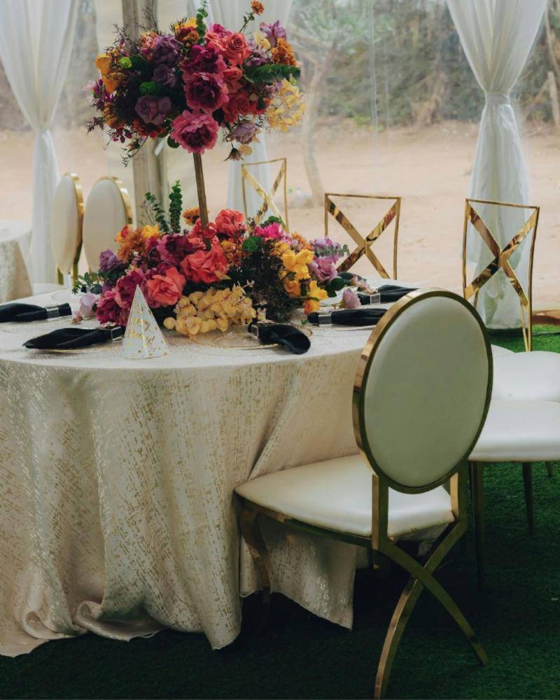 A round table with a tall floral centerpiece and gold chairs at an outdoor event