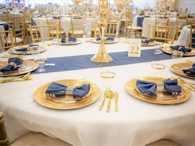 Round table with gold chargers, navy napkins and a gold candelabra